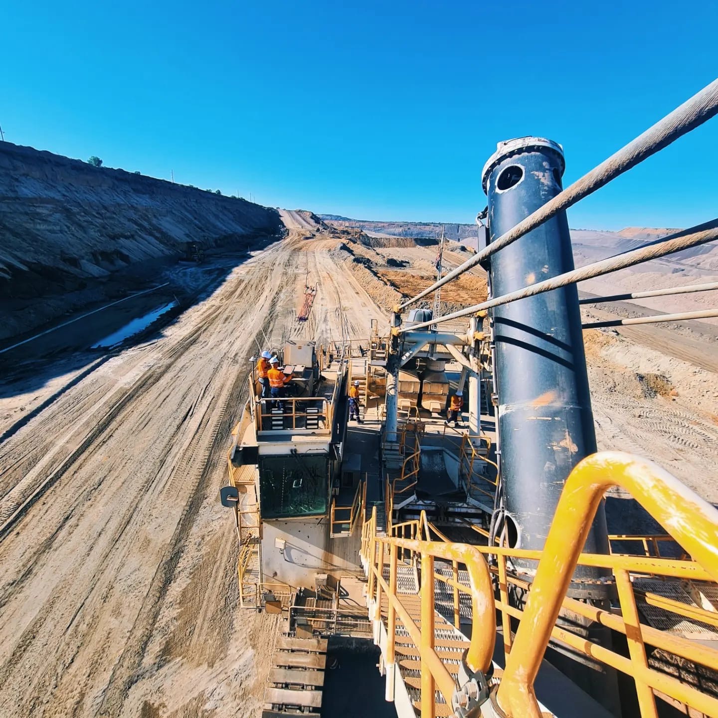 Crew in high-visibility clothing working on the walkway of a dragline above an open-cut strip