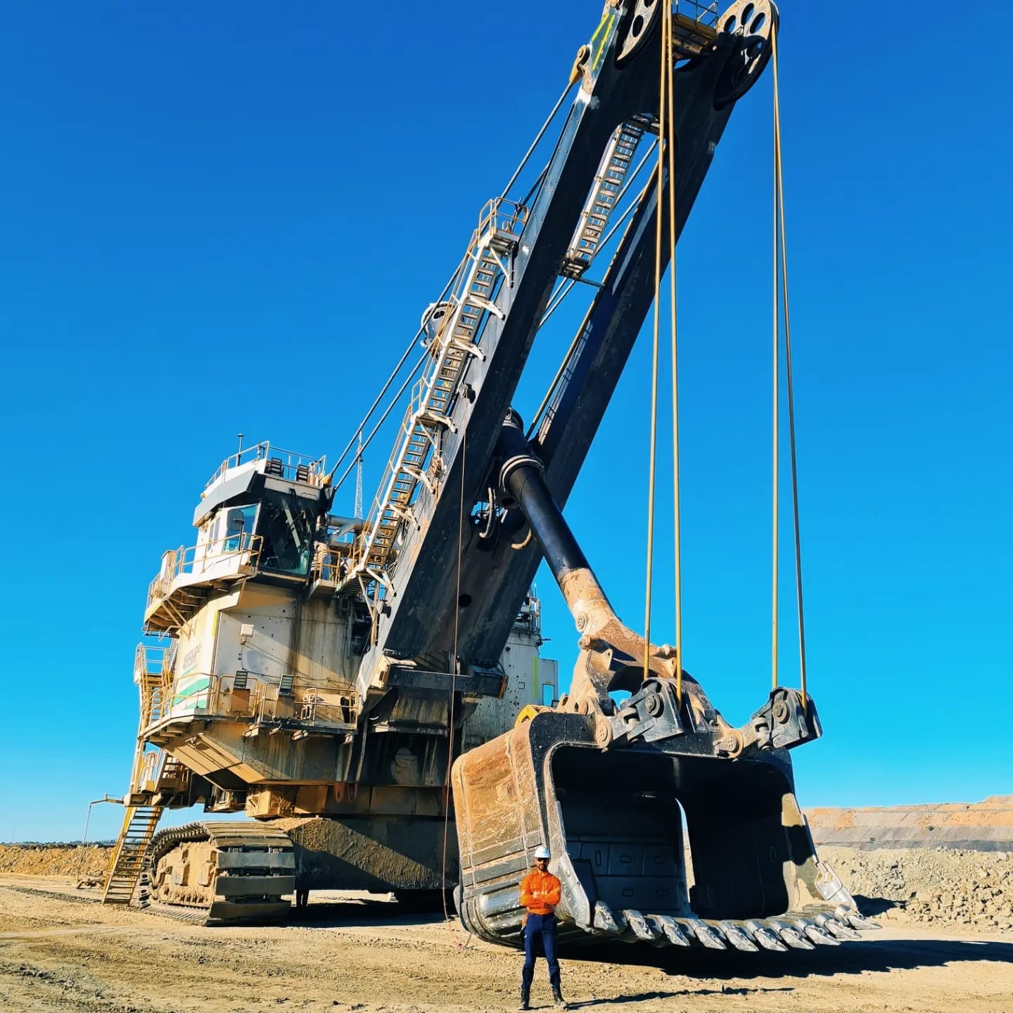 Electric rope shovel with crew member standing beside the bucket, giving scale on a Tier 1 open-cut mine site